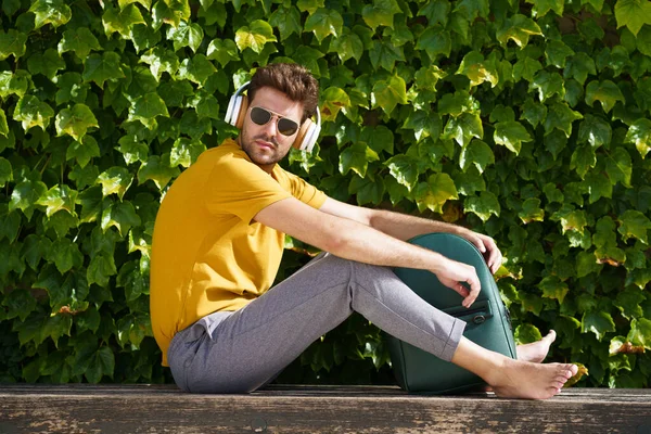 Mladý student sedí venku ve sluchátkách a batohu. — Stock fotografie