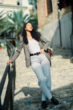 Kendine güvenen genç bir kadın, güzel güneşli bir günün keyfini çıkarırken şık ve şık kıyafetlerini canlı doğayla dolu çarpıcı bir arka plana gururla sergiliyor.