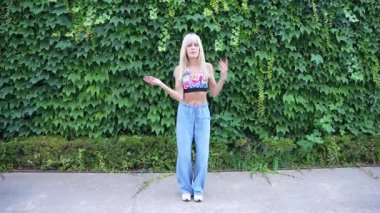 Canlı bir bluz giymiş bir kadın ve bol fildişiyle kaplı bir duvarın önünde etkileyici hareketlerle dans eden kot pantolonlar, neşe saçan, hayat dolu bir yetenek, özgürlük ve yaratıcı ifadenin vücut bulmuş hali.