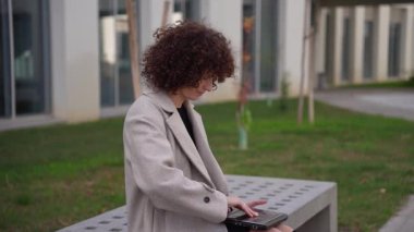 Güzel kıvırcık saçlı bir kadın şık bir bankta huzur içinde ve zarafetle oturur ve yanından geçen herkese huzur ve güzellik getiren sakin ve sakin bir atmosfer yaratır.