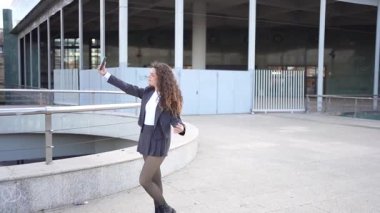 Şık, kendine güvenen genç bir kadın şık, çağdaş bir binanın önünde dolaşırken selfie çekiyor. Şehir keşiflerinin özünü ve kendini ifade etmenin gücünü güzel bir şekilde vurguluyor.