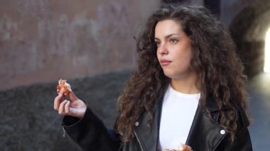 Şık, kıvırcık saçlı genç bir kadın şehir hayatının özünü yansıtan büyüleyici ve pitoresk şehir zeminine karşı çeşitli lezzetli sokak yemeklerinden zevk alıyor.