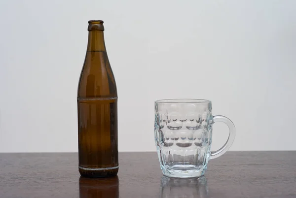 A Dimpled Pint Glass and a Bottle of Beer on a Brown Wooden Table