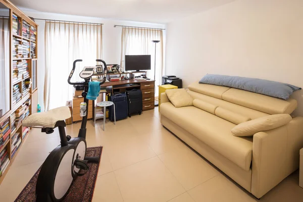 Study with an exercise bike in the middle of the room, leather sofa and bookshelf full of books. nobody inside