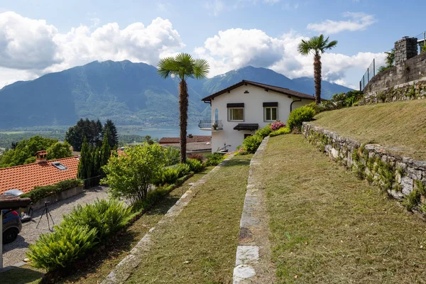 Exterior of villa with large green garden. View of hills and lake. Nobody inside