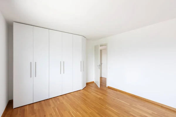 White empty room with large white wardrobe and open door on the corridor. Nobody inside