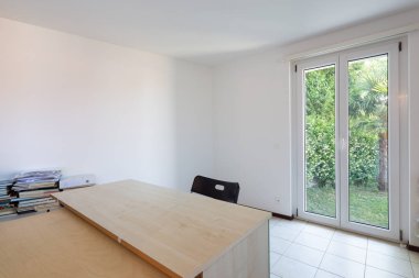 Studio masası, sandalye ve yığılmış belgeleri ile. Bahçeye bakan pencere