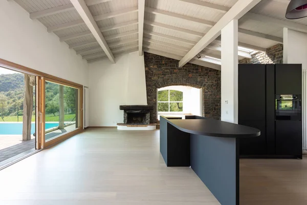 Empty living room with dark kitchen and island, wooden beams