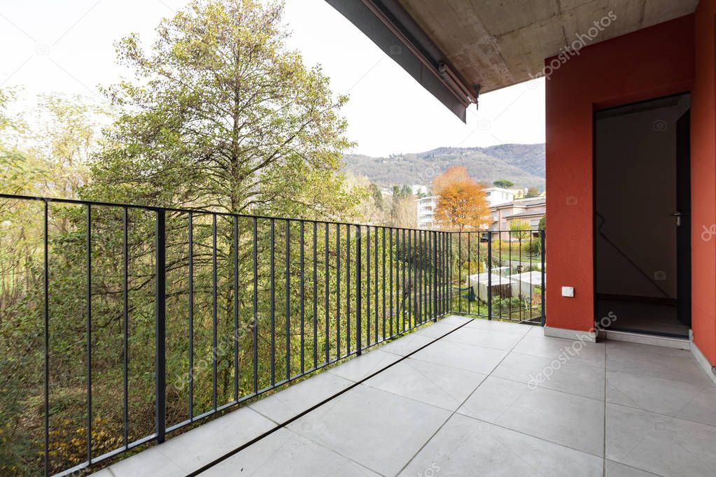 Terrace overlooking nature of apartment with red exterior walls. Nobody inside