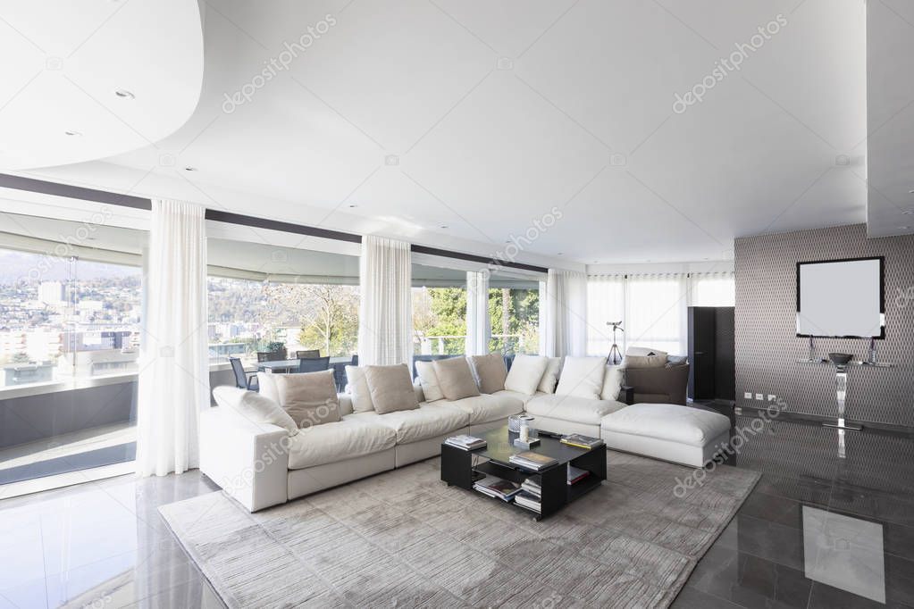 Living room with white leather sofa and windows overlooking the city of Lugano in Switzerland. Nobody inside