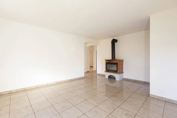 Spacious living room with fireplace and light tiled floor. On the left there is an arched door that leads to the rooms.