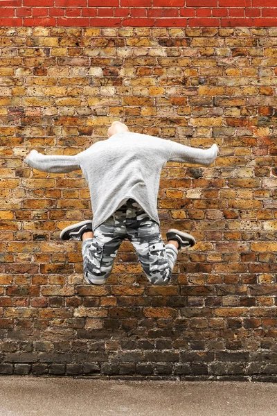 Young girl jumps in front of a brown brick wall — Stock Photo, Image