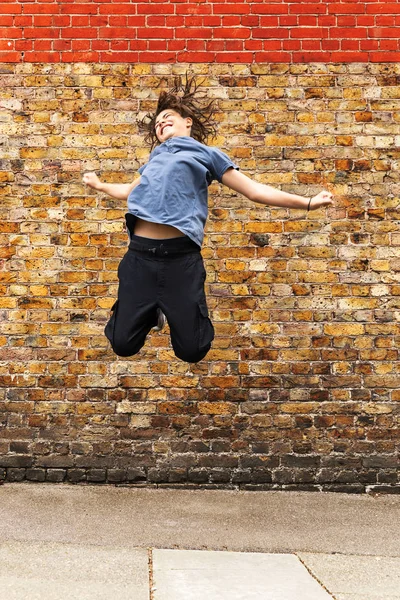 Young boy jumps in front of a brown brick wall — Stock Photo, Image