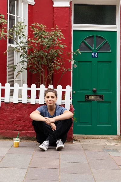 Young boy is sitting outside the home with crossed legs