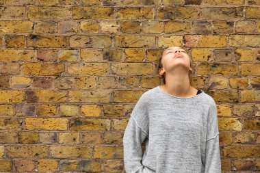 Depresif kız yukarı bakan bir tuğla duvar önünde durmak