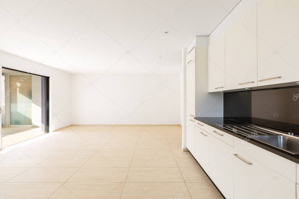 Empty room with white walls, travertine floor and white kitchen 
