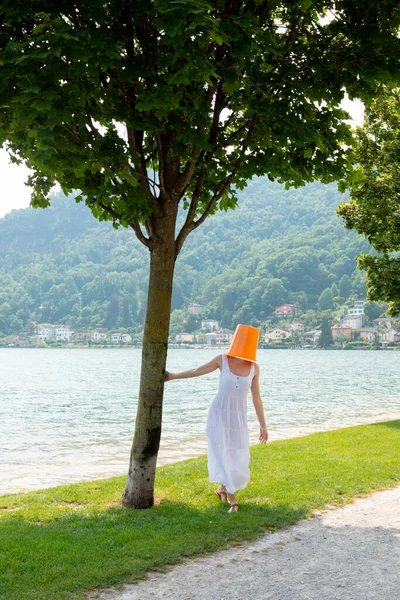 一个年轻的女人站在湖边 头上顶着一个橙色的水桶 穿着一件长裙和一条白裙子 — 图库照片