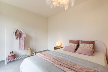 Zarif bir çift kişilik yatak odası. Renkli battaniyeler, yastıklar ve arka planda kurutma askısı.