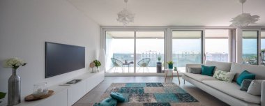 Tasarımcı mobilyalarıyla modern oturma odası. Hafif yastıklı ve balkon manzaralı kanepe. İçeride kimse yok. Ön manzara, panorama