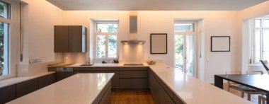 Pencere ve parke olan bir villada modern bir mutfak. Beyaz tezgah ve kahverengi kapılar. İçeride kimse yok.