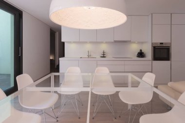 Tasarımcı sandalyeli ön cam masa. Beyaz, minimal, modern mutfak. İçeride kimse yok.