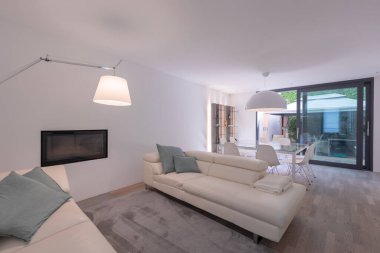 Açık deri koltukları, asılı bir lambası, şöminesi ve parlak bir penceresi olan oturma odası. İçeride kimse yok.