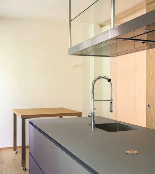 Modern kitchen with suspended hood, large sink, oven and wooden worktop. Detail of modern tap. Nobody inside