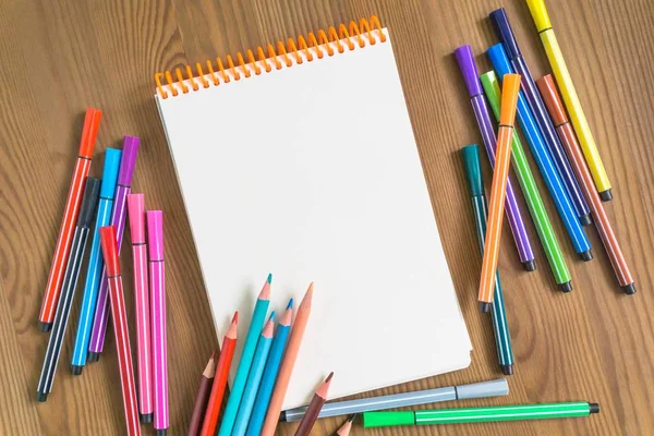 parlak renkli kalemler ve işaretleyiciler yanındaki ahşap bir masa üzerinde bir eskiz defteri