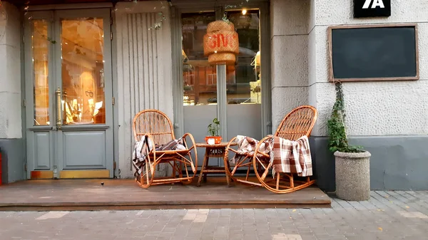 Wicker cozy armchair with blanket and small glass table outdoors. Plaid lies on the wicker furniture from rattan. — Stock Photo, Image