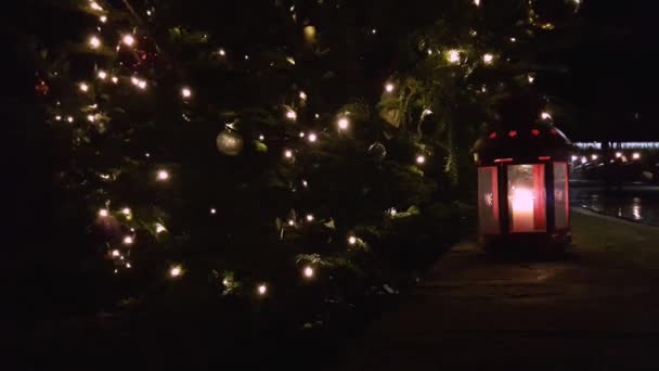 Primer plano de la linterna de Navidad. La linterna roja de Navidad se encuentra unde debajo de un abeto de Navidad. Linterna con vela encendida en la nieve por la noche. Foto teñida — Vídeo de stock