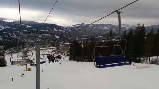 Teleférico en las montañas para esquiadores en la estación de esquí. Telesilla. La gente sube al ascensor en la estación de esquí. Esquiadores y snowboarders bajan por la pista . — Vídeos de Stock