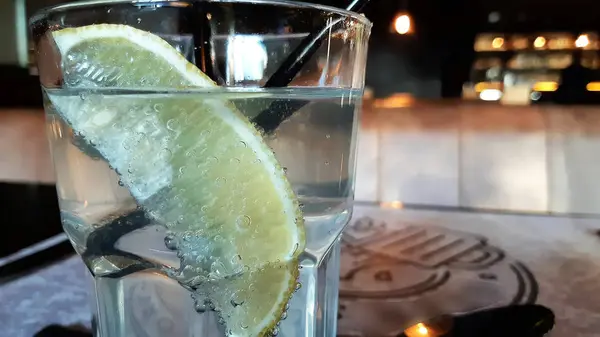 Eine Orangenscheibe in einem Glas mit sprudelndem Wasser. ein Glas Wasser mit einer Zitronenscheibe, — Stockfoto