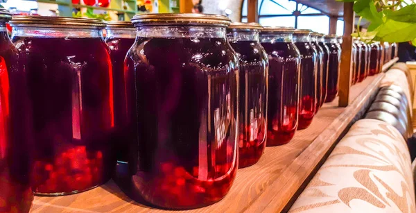 Canned fruit drinks in glass jars. Compote of berries in jars. Several Colorful cans of compote on a wooden shelf. Selective focus. Shallow depth of field.