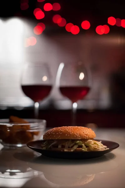 Romantik bir akşam yemeği: iki kadeh şarap ve jucy hamburger, nuggets çoğu yılbaşı ışıkları ile koyu arka plan