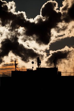 Bir gökdelenin çatısında çanak antenler ile bir Bağıntı antenler siluetleri ile gündoğumu