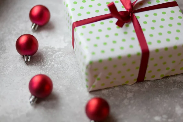 Décorations de Noël sur fond gris. Boîte blanche et verte floue avec un nœud bordeaux entouré de boules de Noël bordeaux, de jouets de Noël et d'ornements en pierre. Vue du dessus . — Photo