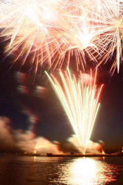 Suyun üstünde yeni yıl havai fişekleri kara gökyüzünü yansıtıyor. 