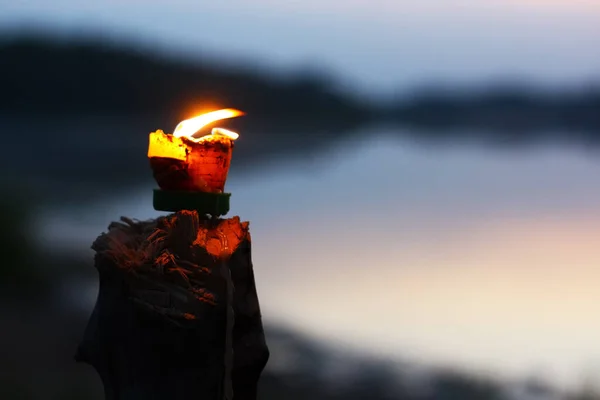 Lilin cahaya dengan api panas menyala terang di blur gelap tepi laut gelap tepi sungai reflektif gelombang riak latar belakang pasang: hangat twilight awan langit dengan tepi sungai air — Stok Foto