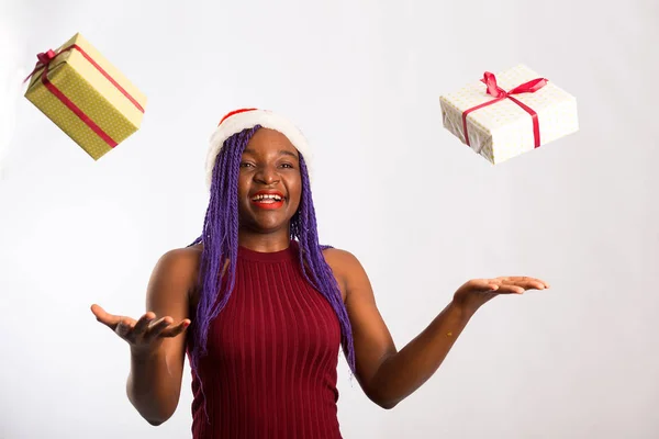 Krásná afro americká dívka v šatech a Santa klobouk je chytání padající dárky, při pohledu na kameru a usmívání, izolované na bílém pozadí — Stock fotografie