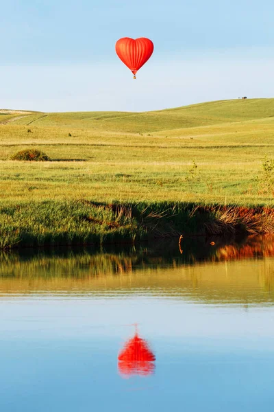 心形的热气球降落在湖后的落日中 映衬着湖中的景象 — 图库照片
