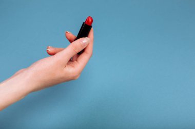 Kadının eli kırmızı ruj alıyor. Mavi arkaplanda izole edilmiş.