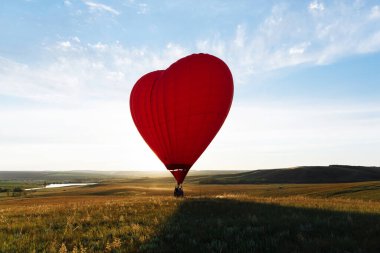 Sıcak kırmızı hava balonu kalp şekli vadi üzerinde gün batımına doğru uçuyor ya da kalkıyor.