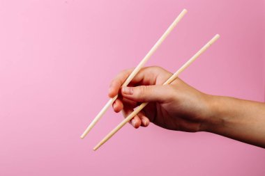 Elleri yemek çubuğu tutuyordu. Pembe arkaplanda izole edilmiş, başlık ve metin için yer.