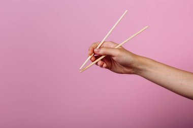 Elleri yemek çubuğu tutuyordu. Pembe arkaplanda izole edilmiş, başlık ve metin için yer.