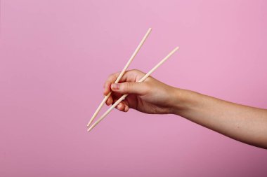 Elleri yemek çubuğu tutuyordu. Pembe arkaplanda izole edilmiş, başlık ve metin için yer.