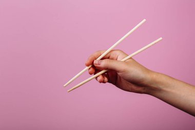 Elleri yemek çubuğu tutuyordu. Pembe arkaplanda izole edilmiş, başlık ve metin için yer.