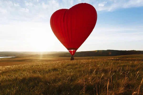 Hot Red air balloon heart shape flying into sunset over valley landing or taking off — Stock Photo, Image