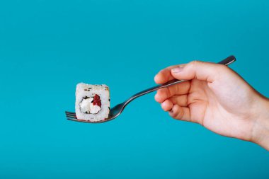 Mavi arka planda izole edilmiş çatallı taze suşi rulosu. Çubuksuz suşi nasıl yenir?.