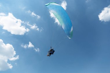 Mavi Paraglider güneşli bir günde bulutlarla gökyüzüne uçuyor.