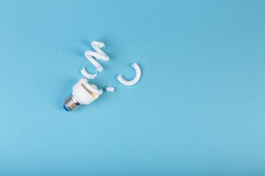 Ekoloji kirliliği kavramı: mavi arka planda ölü incir yapraklarıyla çevrili kırık floresan spiral lamba enerji tasarrufu lambası. Dikkat, zehirli gazlar. Başlık için boşluk.